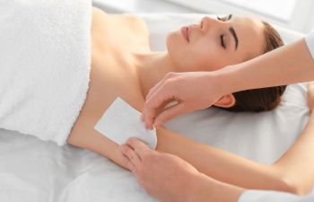 Beautician waxing female armpits in medi spa center