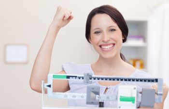 woman happy with weight loss treament results standing on scales and showing a gesture of victory